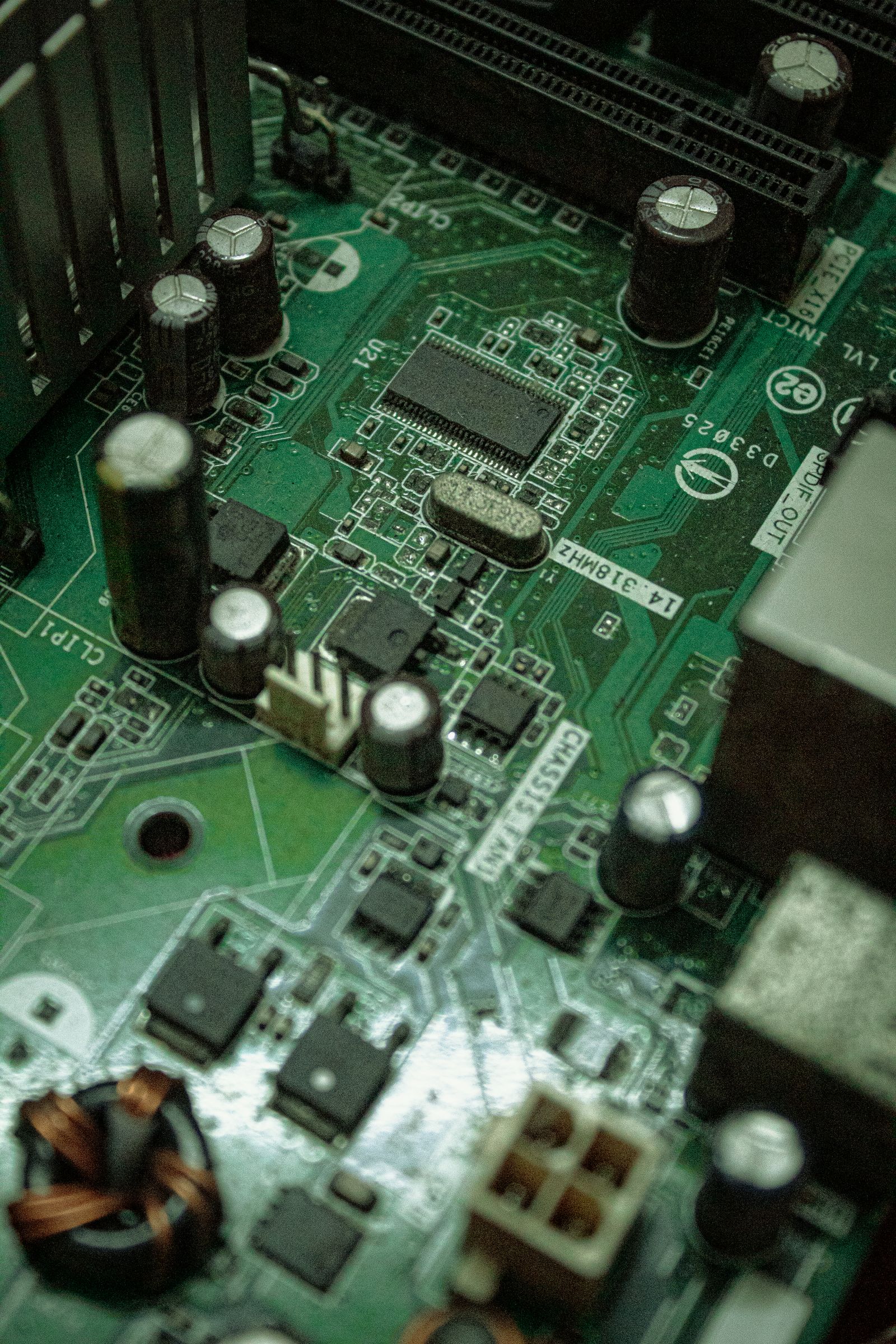 Close-up de uma placa-mãe verde com chips, capacitores e pequenas marcações.