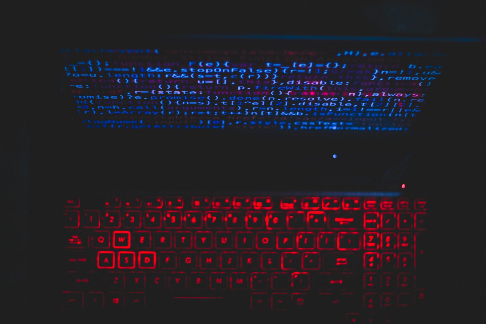Notebook escuro com teclado retroiluminado em vermelho e código azul refletido na tela.
